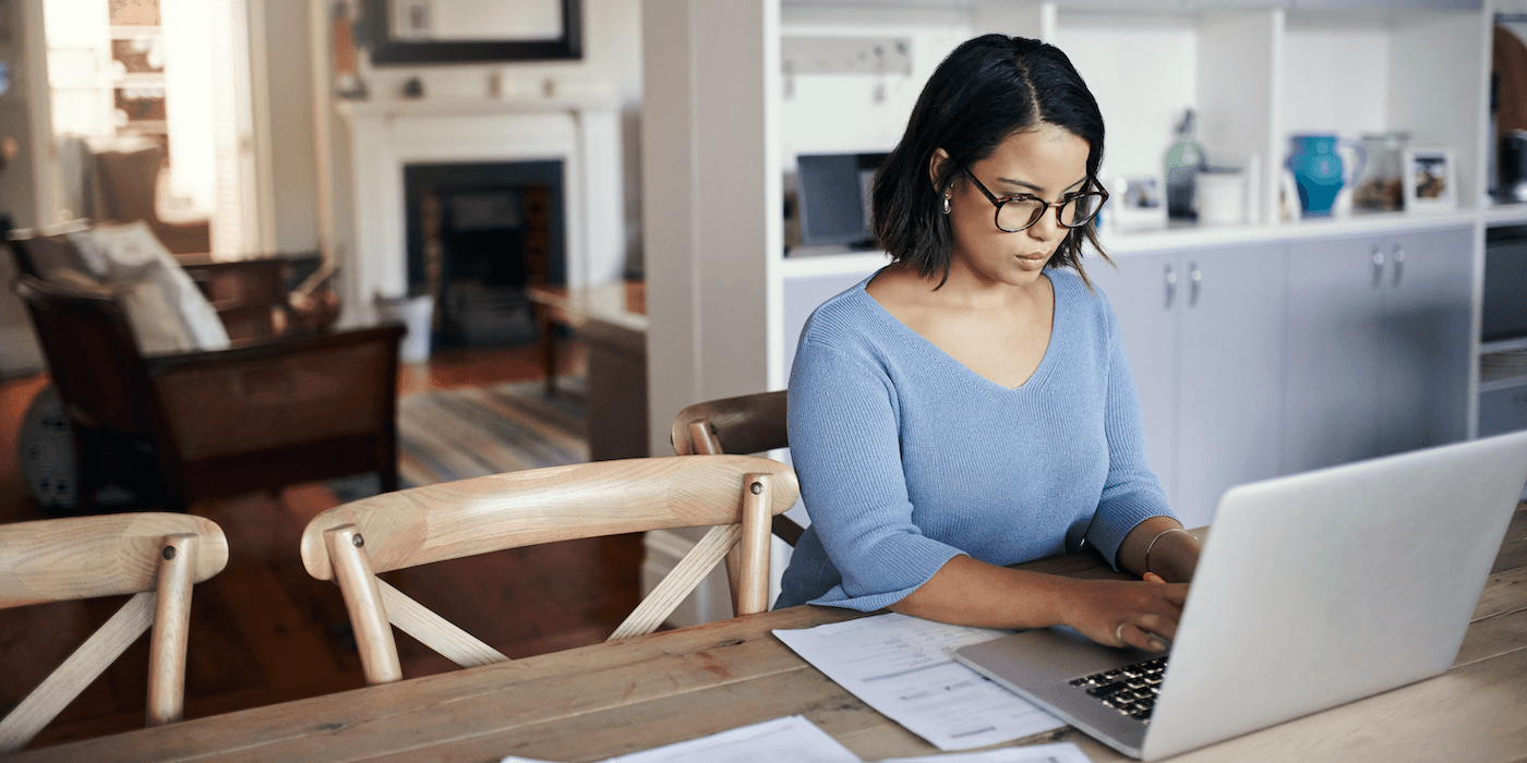 person sitting at home at kitchen table typing on a laptop