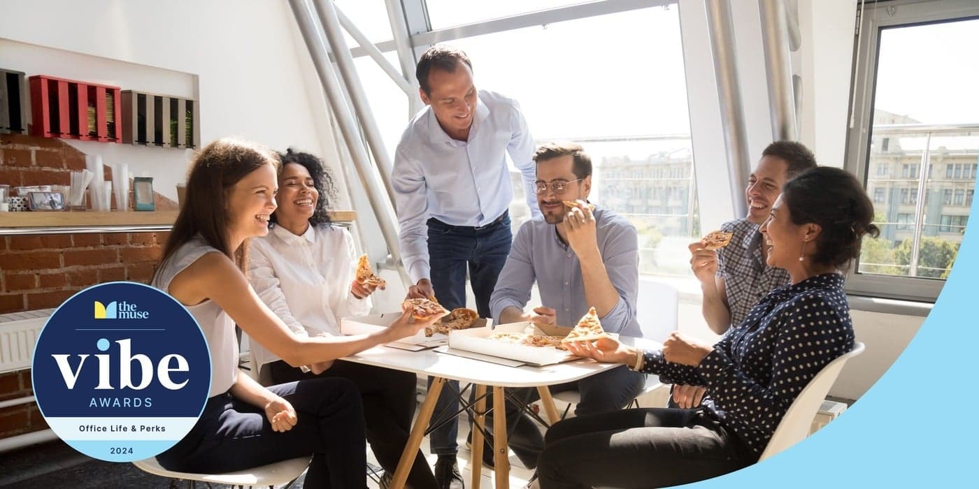 A team of coworkers smiling and eating pizza around a table