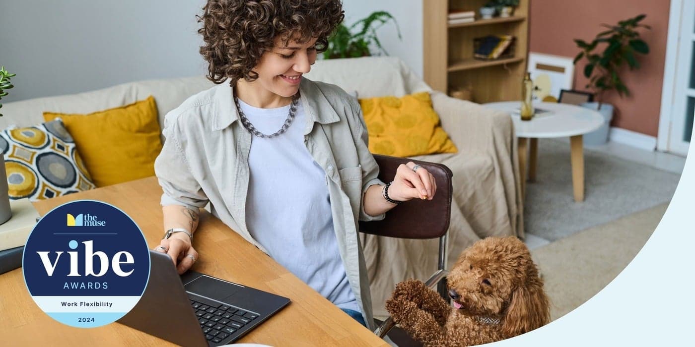 A woman smiling at her dog as she works on a laptop at home