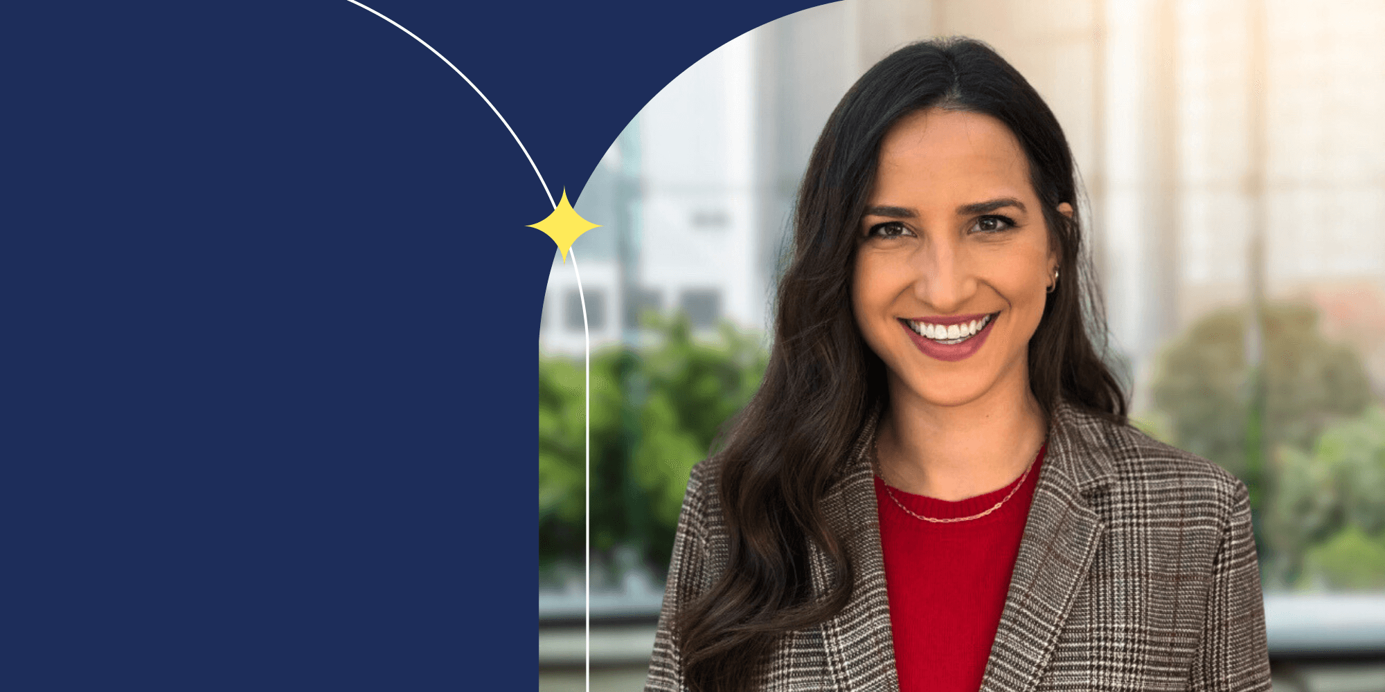 A smiling person facing the camera. They're wearing a gold necklace, red shirt, and plaid blazer. They have long brown hair.